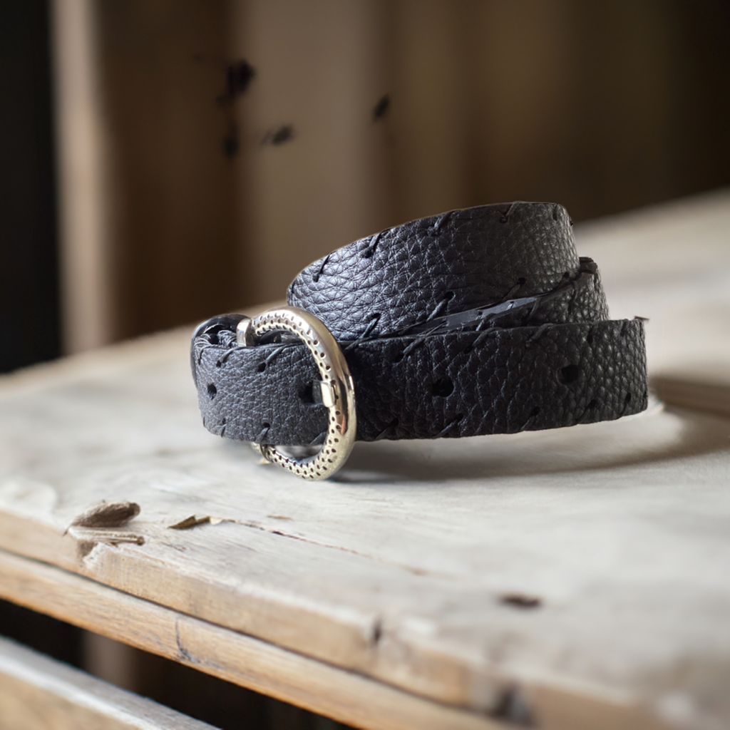 Cintura pelle artigianale nera di Gemelle Toscane su un tavolo di legno, con fibbia elegante