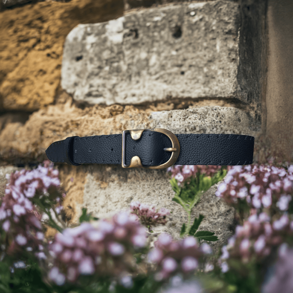 Cintura pelle artigianale nera con fibbia in metallo su sfondo di pietre e fiori