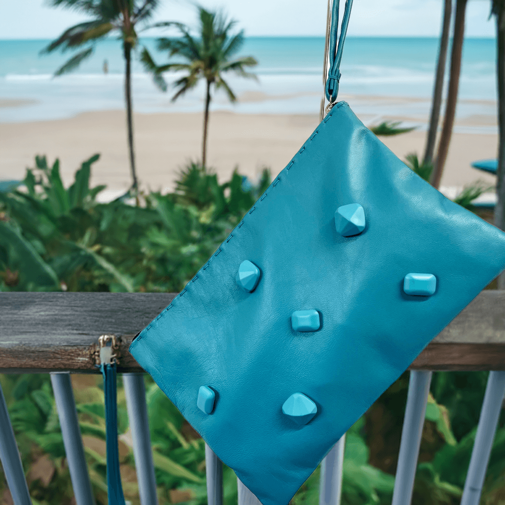 Pochette artigianale in pelle blu con dettagli in rilievo su sfondo tropicale